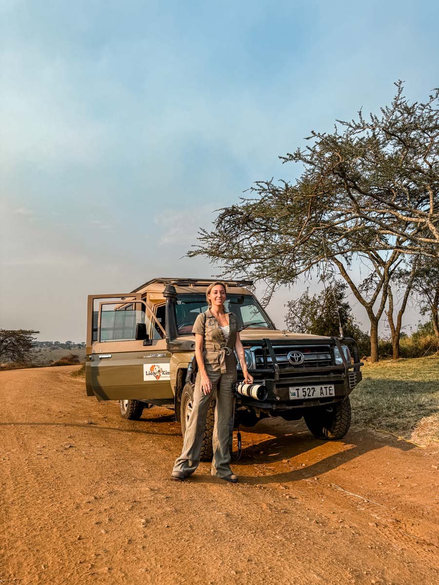 Sam standing in front of the Safari Jeep wearing an olive green jumpsuit and boots.
