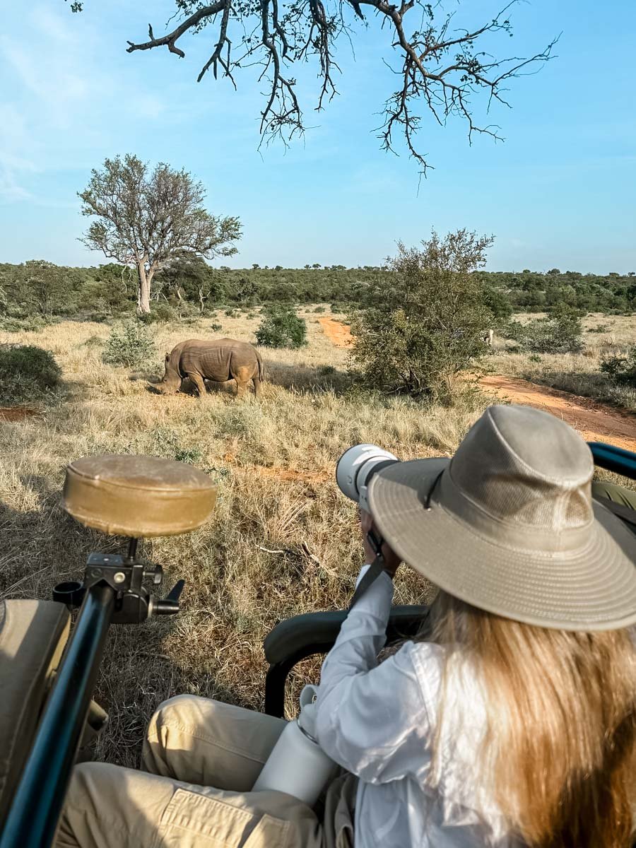 Sam photographing a Rhino wearing a white safari shirt, safari hat and tan pants.